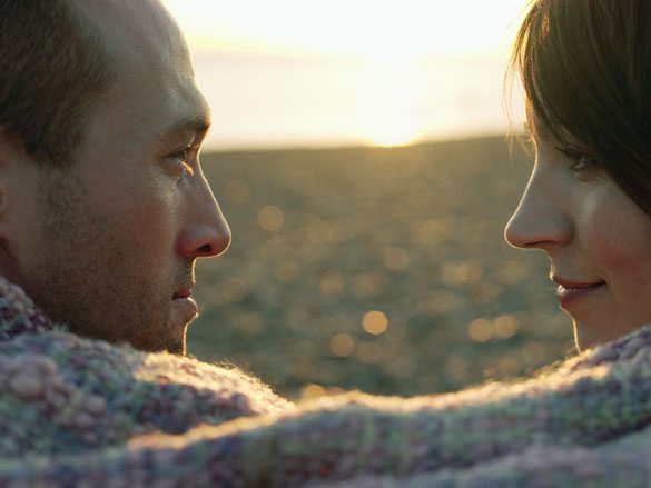 Closeup side view of a couple looking at each other wrapped in blanket on beach