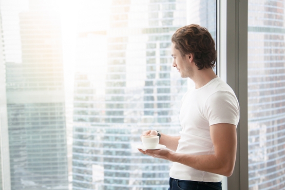 Young handsome carefree Taurus man near modern full length window enjoying a cup of coffee while looking outside - How Can You Make A Taurus Man Miss You