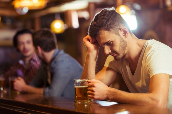 Sad young man in white t-shirt is looking at glass of beer while sitting at bar counter in pub - Why Are Taurus Men So Emotional